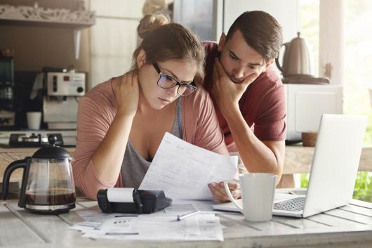 A young couple looking at bills in a kitchen setting. 