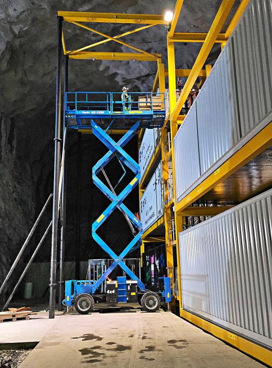 An elevated lift in front of large containers. 